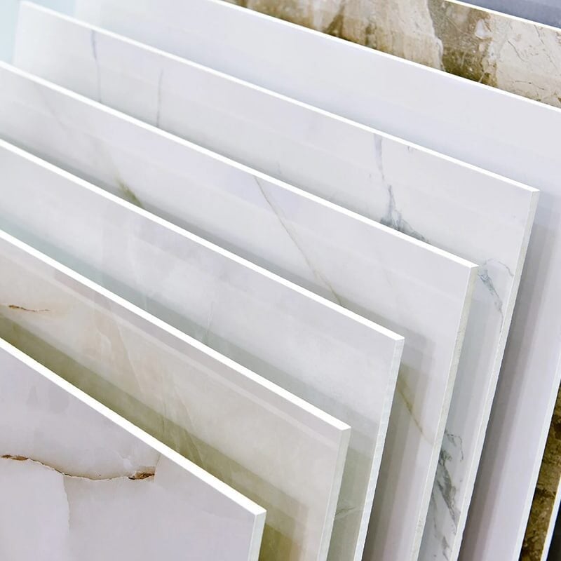 Several large rectangular slabs of tile or stone are displayed upright in a row, showcasing various shades and marble-like patterns—perfect examples of stylish water resistant flooring for any space.